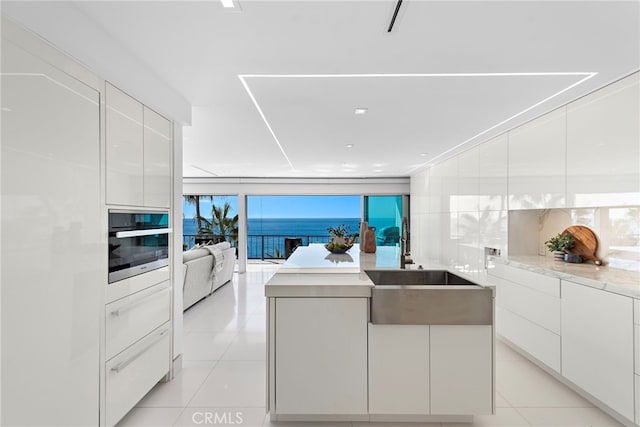 kitchen featuring floor to ceiling windows, stainless steel oven, light tile patterned floors, a water view, and white cabinets