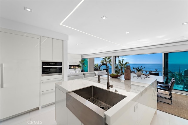 kitchen with light stone countertops, sink, oven, a water view, and white cabinets