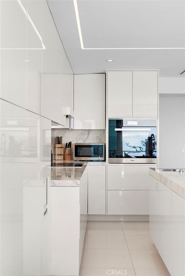 kitchen featuring white cabinets, light tile patterned flooring, backsplash, and appliances with stainless steel finishes