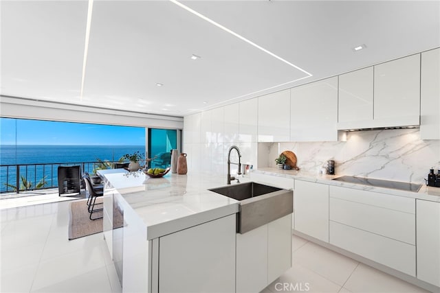 kitchen featuring backsplash, a water view, black electric cooktop, a healthy amount of sunlight, and white cabinetry