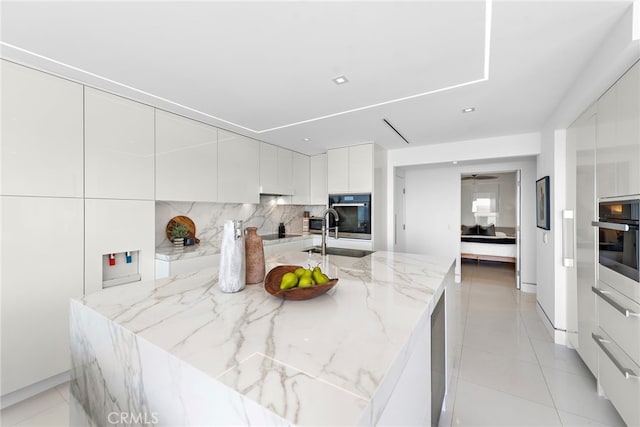 kitchen featuring light stone countertops, tasteful backsplash, sink, light tile patterned floors, and white cabinets