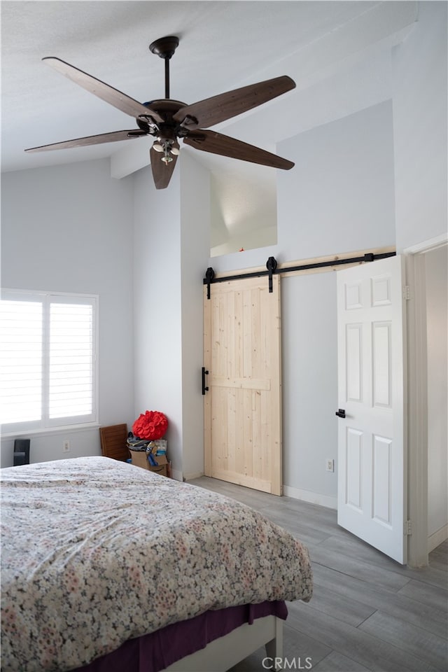 bedroom with a barn door, hardwood / wood-style flooring, high vaulted ceiling, and ceiling fan