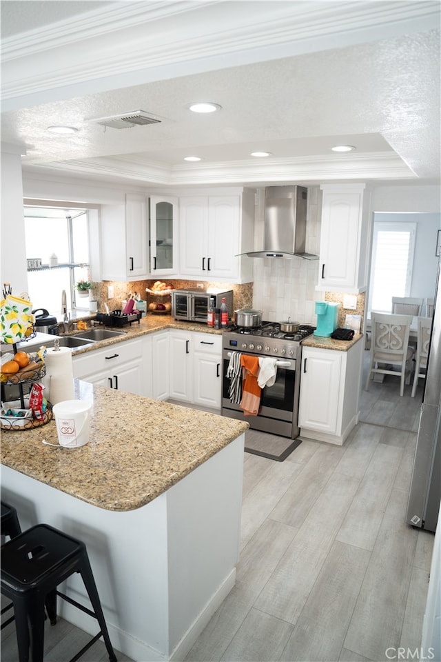 kitchen featuring wall chimney exhaust hood, white cabinets, plenty of natural light, and high end stainless steel range