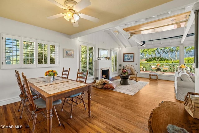 dining room with ceiling fan, wood-type flooring, and vaulted ceiling with beams