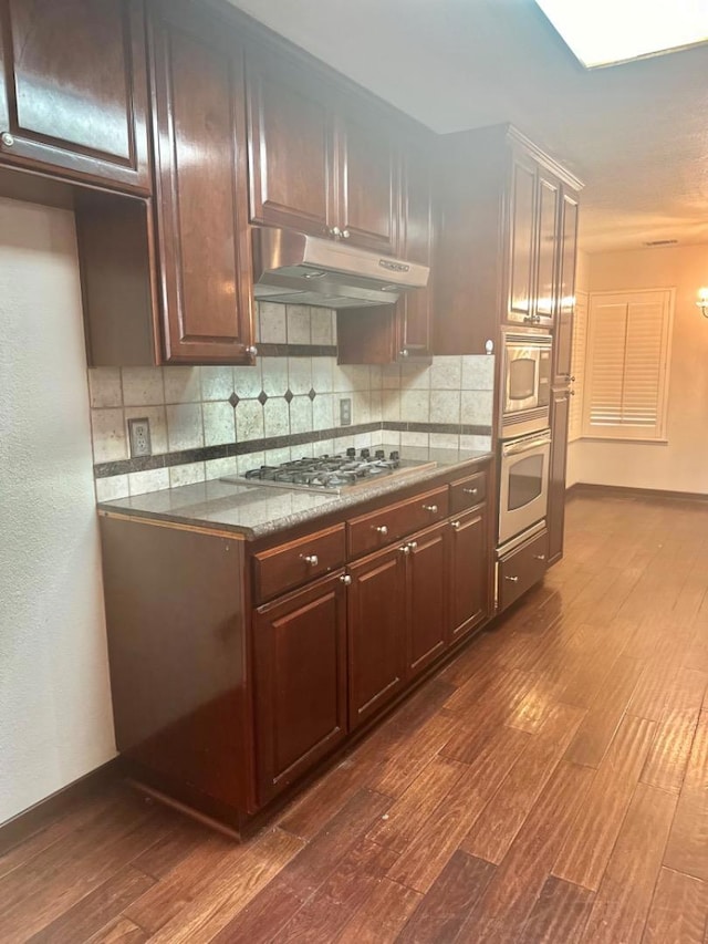 kitchen featuring tasteful backsplash, dark brown cabinets, stainless steel appliances, and dark wood-type flooring