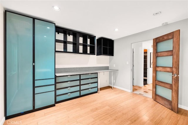 unfurnished bedroom with a closet, built in desk, and light hardwood / wood-style flooring