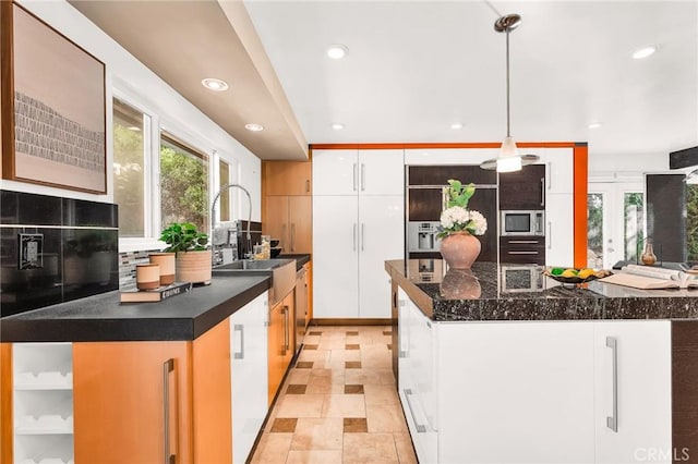 kitchen with pendant lighting, a center island, stainless steel microwave, backsplash, and white cabinetry