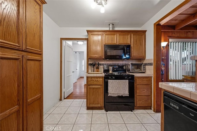 kitchen featuring tasteful backsplash, tile counters, light tile patterned flooring, and black appliances