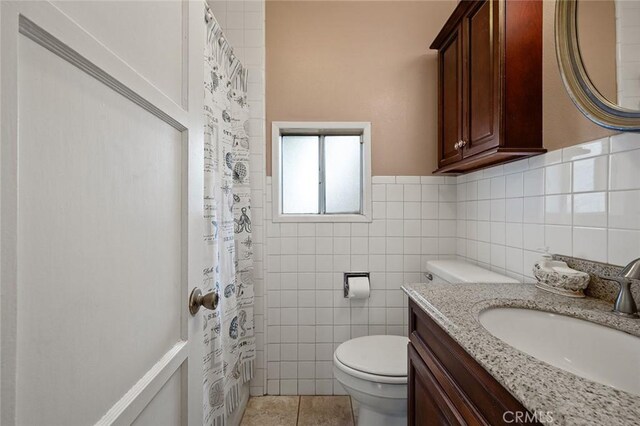 bathroom featuring tile patterned flooring, vanity, toilet, and tile walls