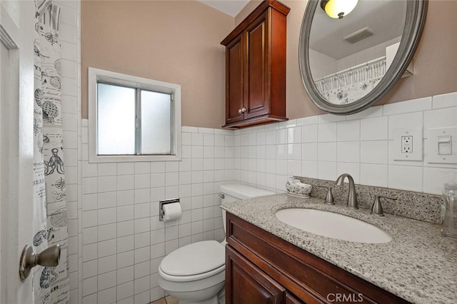 bathroom with curtained shower, vanity, tile walls, and toilet