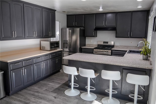 kitchen with a kitchen breakfast bar, kitchen peninsula, hardwood / wood-style floors, sink, and appliances with stainless steel finishes