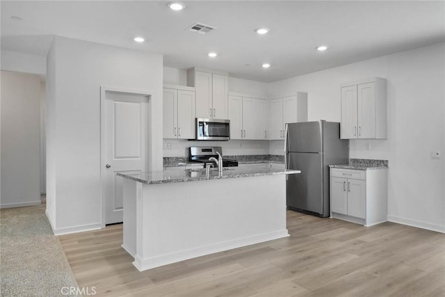 kitchen featuring light stone countertops, light hardwood / wood-style flooring, a kitchen island with sink, white cabinets, and appliances with stainless steel finishes