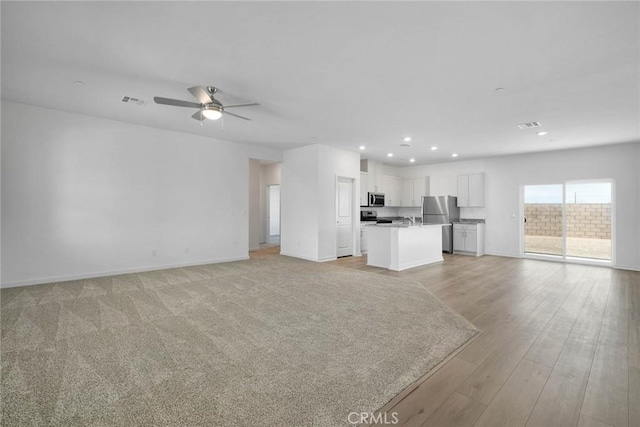 unfurnished living room featuring light hardwood / wood-style floors, ceiling fan, and sink