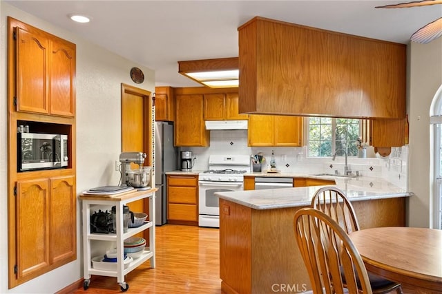 kitchen with kitchen peninsula, appliances with stainless steel finishes, tasteful backsplash, sink, and light hardwood / wood-style floors