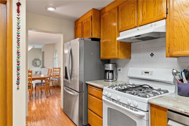 kitchen featuring backsplash, stainless steel fridge, light wood-type flooring, white gas range, and light stone counters