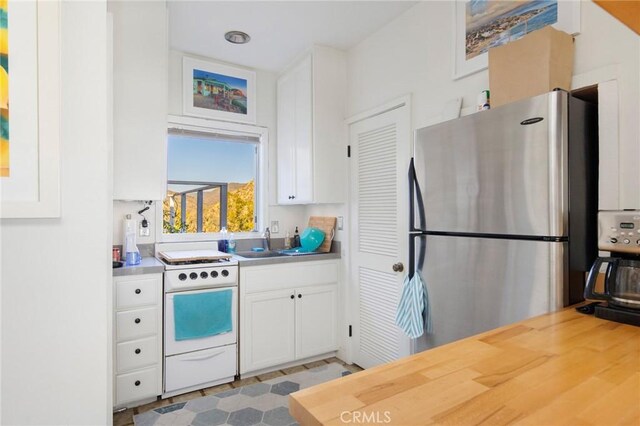 kitchen featuring electric stove, white cabinets, sink, and stainless steel refrigerator