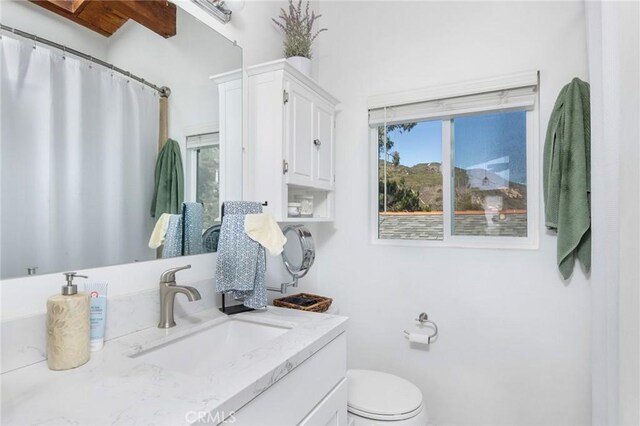 bathroom with toilet, beam ceiling, plenty of natural light, and vanity