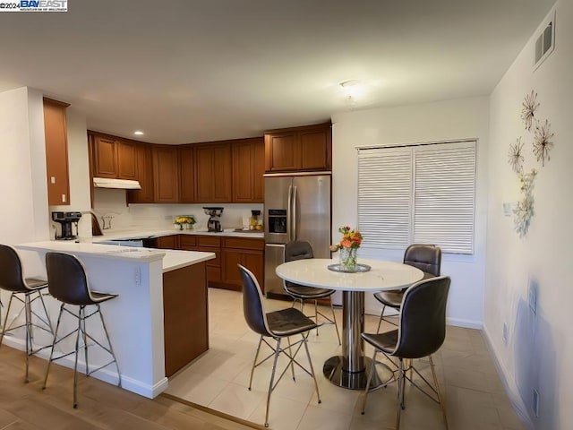 kitchen with a kitchen breakfast bar, kitchen peninsula, sink, and stainless steel refrigerator with ice dispenser