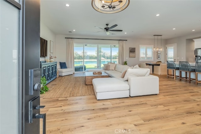 living room featuring light wood-type flooring and ceiling fan with notable chandelier