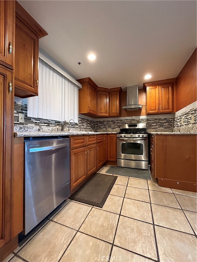 kitchen featuring wall chimney range hood, light tile patterned floors, appliances with stainless steel finishes, light stone counters, and tasteful backsplash