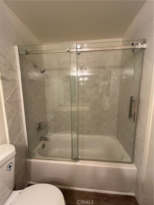 bathroom with bath / shower combo with glass door, a textured ceiling, and toilet