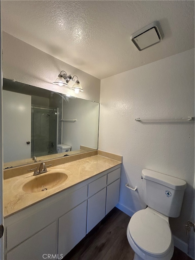 bathroom with a textured ceiling, an enclosed shower, toilet, vanity, and hardwood / wood-style flooring