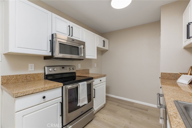 kitchen with white cabinets, sink, appliances with stainless steel finishes, light hardwood / wood-style floors, and light stone counters