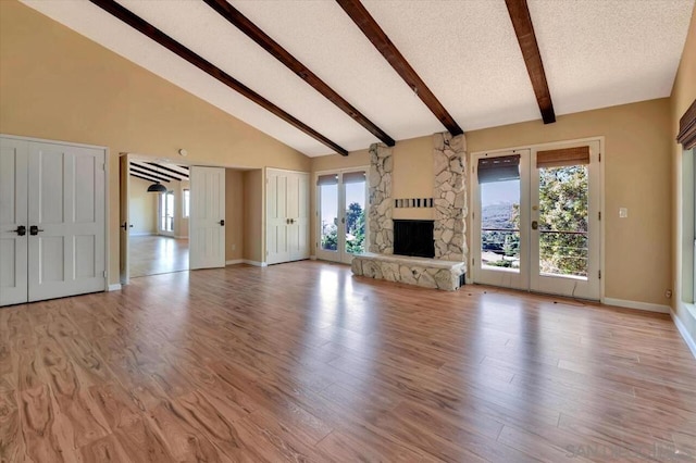 unfurnished living room featuring light hardwood / wood-style floors, high vaulted ceiling, a stone fireplace, and french doors