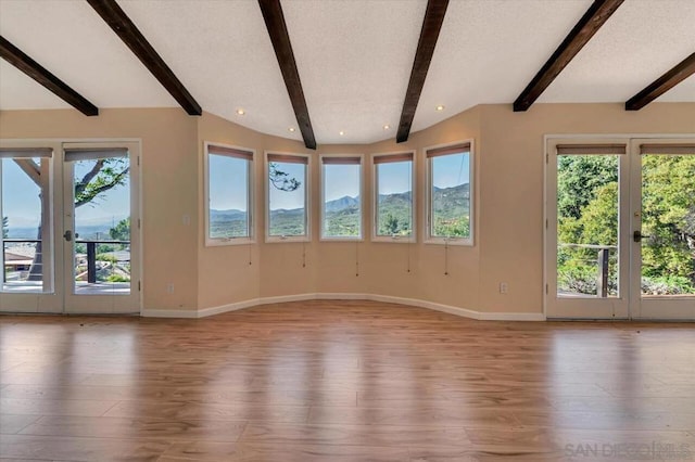 unfurnished living room with a mountain view, light hardwood / wood-style flooring, beam ceiling, and a healthy amount of sunlight