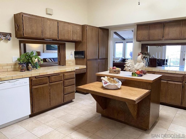 kitchen with white dishwasher, light tile patterned floors, dark brown cabinetry, and tile counters