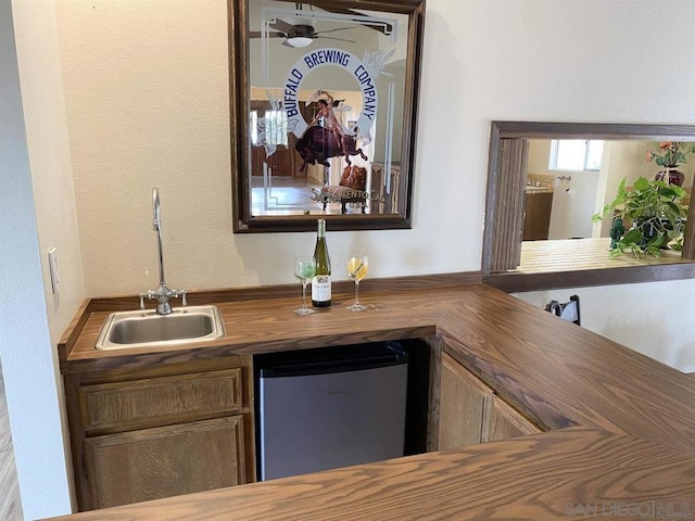 bar featuring sink, stainless steel fridge, ceiling fan, and wooden counters