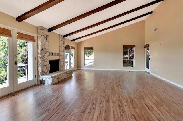 unfurnished living room with high vaulted ceiling, hardwood / wood-style floors, beam ceiling, and a stone fireplace