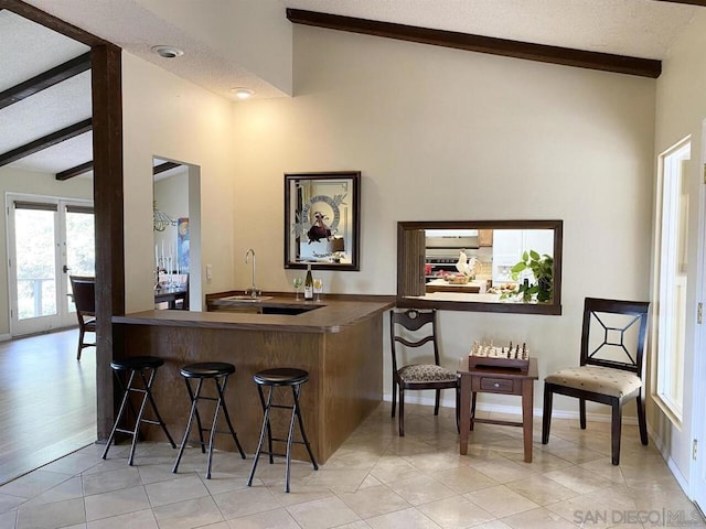 kitchen with a textured ceiling, light tile patterned floors, a kitchen breakfast bar, kitchen peninsula, and lofted ceiling with beams