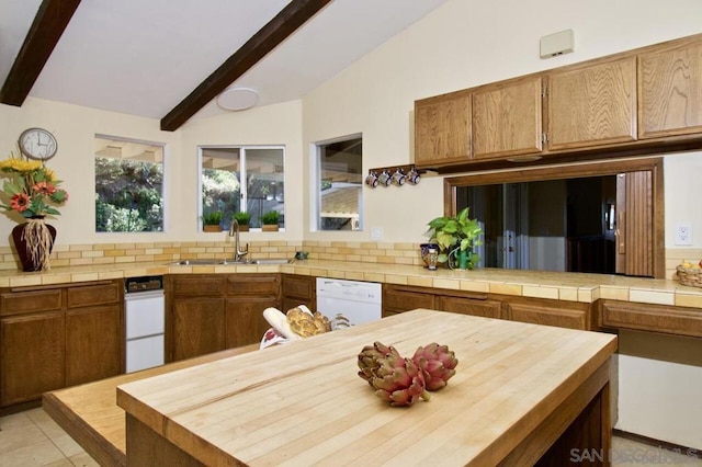 kitchen with white dishwasher, sink, vaulted ceiling with beams, backsplash, and light tile patterned flooring