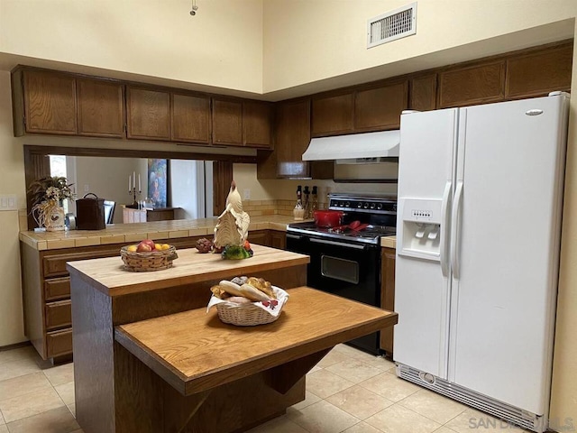 kitchen with white fridge with ice dispenser, dark brown cabinetry, electric range, kitchen peninsula, and light tile patterned flooring