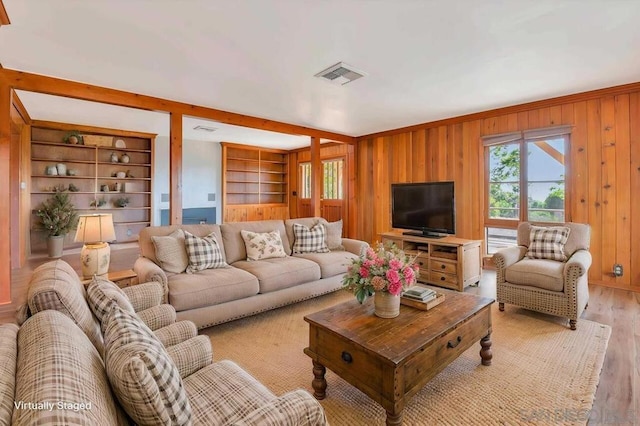 living room with built in features, light hardwood / wood-style floors, and wood walls