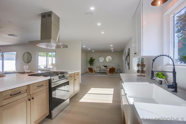 kitchen with sink, light wood-type flooring, wall chimney exhaust hood, stainless steel gas range, and light brown cabinets