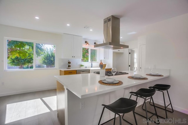 kitchen featuring kitchen peninsula, island exhaust hood, white cabinets, appliances with stainless steel finishes, and a breakfast bar