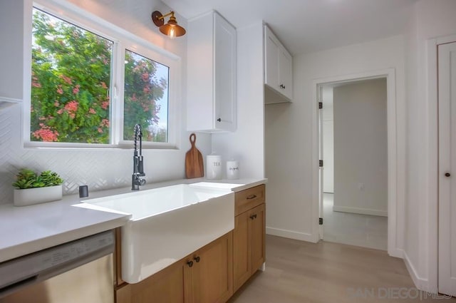 kitchen featuring sink, light wood-type flooring, white dishwasher, white cabinets, and decorative backsplash