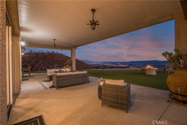 patio terrace at dusk with a mountain view, outdoor lounge area, a yard, and ceiling fan