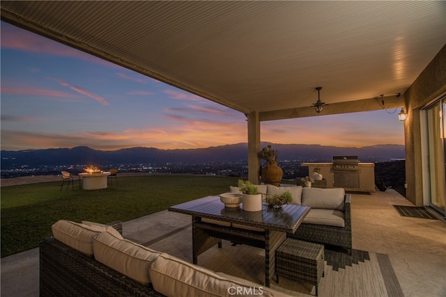 patio terrace at dusk featuring a mountain view, area for grilling, a lawn, and an outdoor hangout area