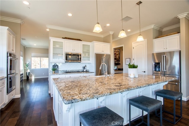 kitchen with a large island with sink, dark wood-type flooring, stainless steel appliances, decorative light fixtures, and white cabinetry