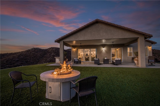 back house at dusk featuring a yard, an outdoor living space with a fire pit, and a patio