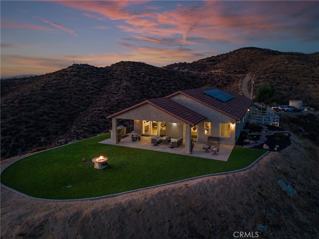 back house at dusk with a patio, a mountain view, and a lawn