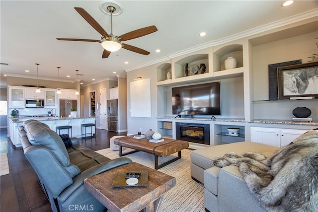 living room featuring sink, built in features, light hardwood / wood-style floors, ceiling fan, and crown molding