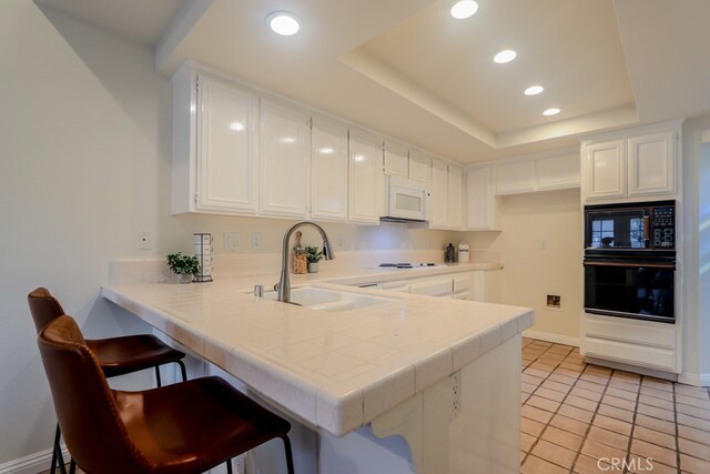 kitchen with kitchen peninsula, sink, black appliances, a breakfast bar, and white cabinets