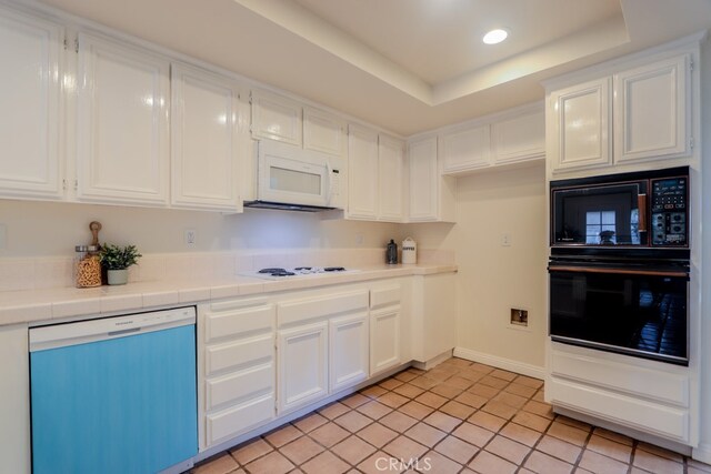 kitchen featuring tile counters, a tray ceiling, black appliances, light tile patterned flooring, and white cabinetry