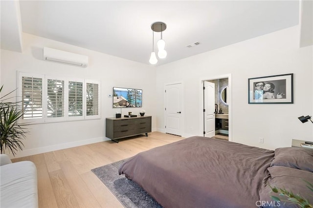 bedroom with ensuite bathroom, a wall mounted air conditioner, and light wood-type flooring