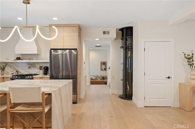 kitchen featuring light brown cabinetry, stainless steel refrigerator, a kitchen bar, range, and light wood-type flooring