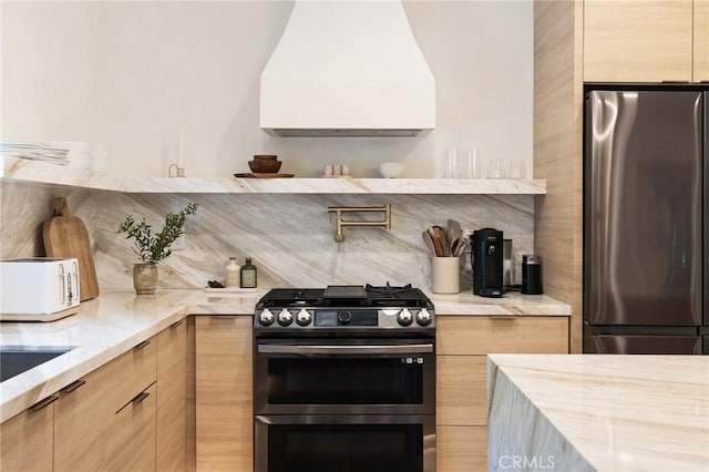 kitchen with appliances with stainless steel finishes, custom range hood, light stone counters, and light brown cabinetry